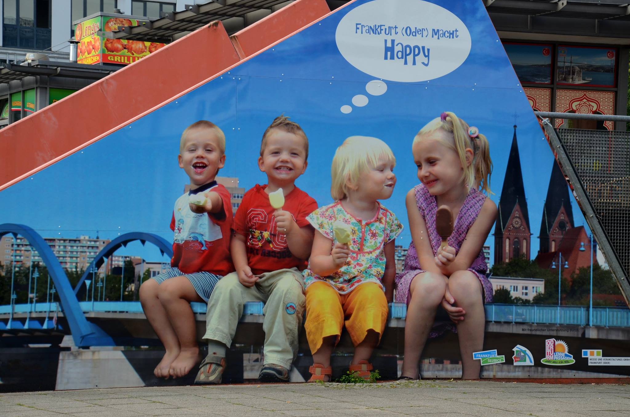 Ein Poster an der Wand, vier Kinder essen Eis mit Stiel und lächeln, in der Wolke ein Text: "Frankfurt (Oder) macht Happy"