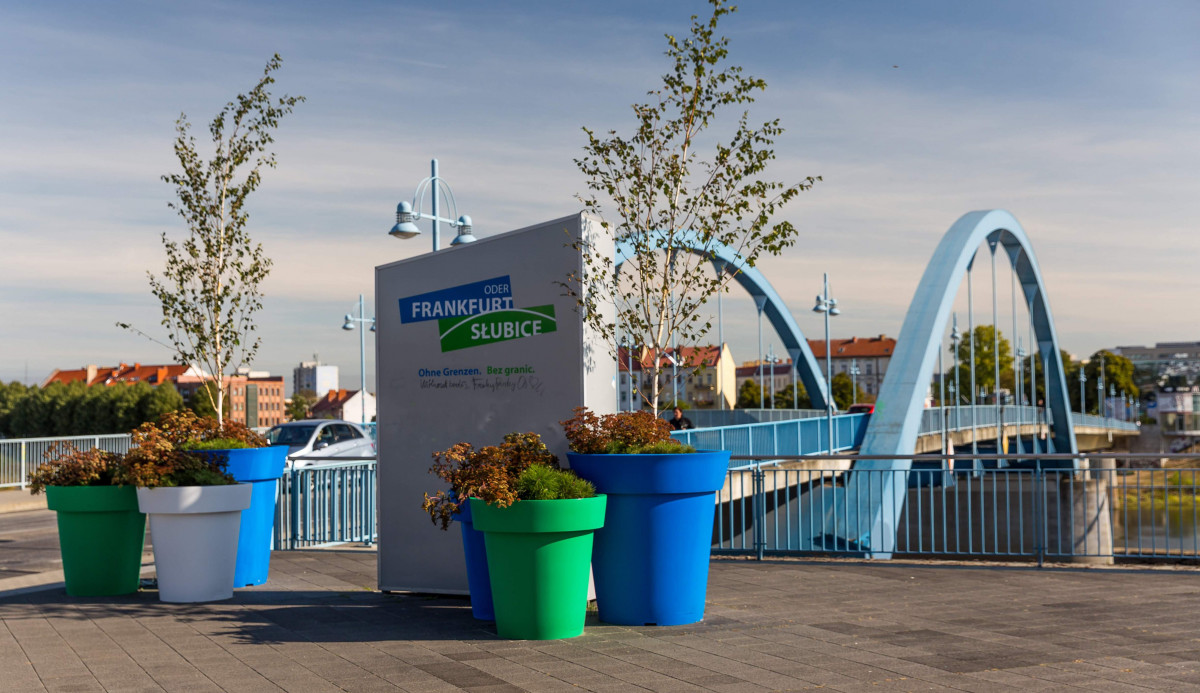 Blick auf die Stadttafel: Frankfurt (Oder) und Slubice: Ohne Grenzen, die an der Stadtbrücke umgeben von großen Pflanzenkübel steht.