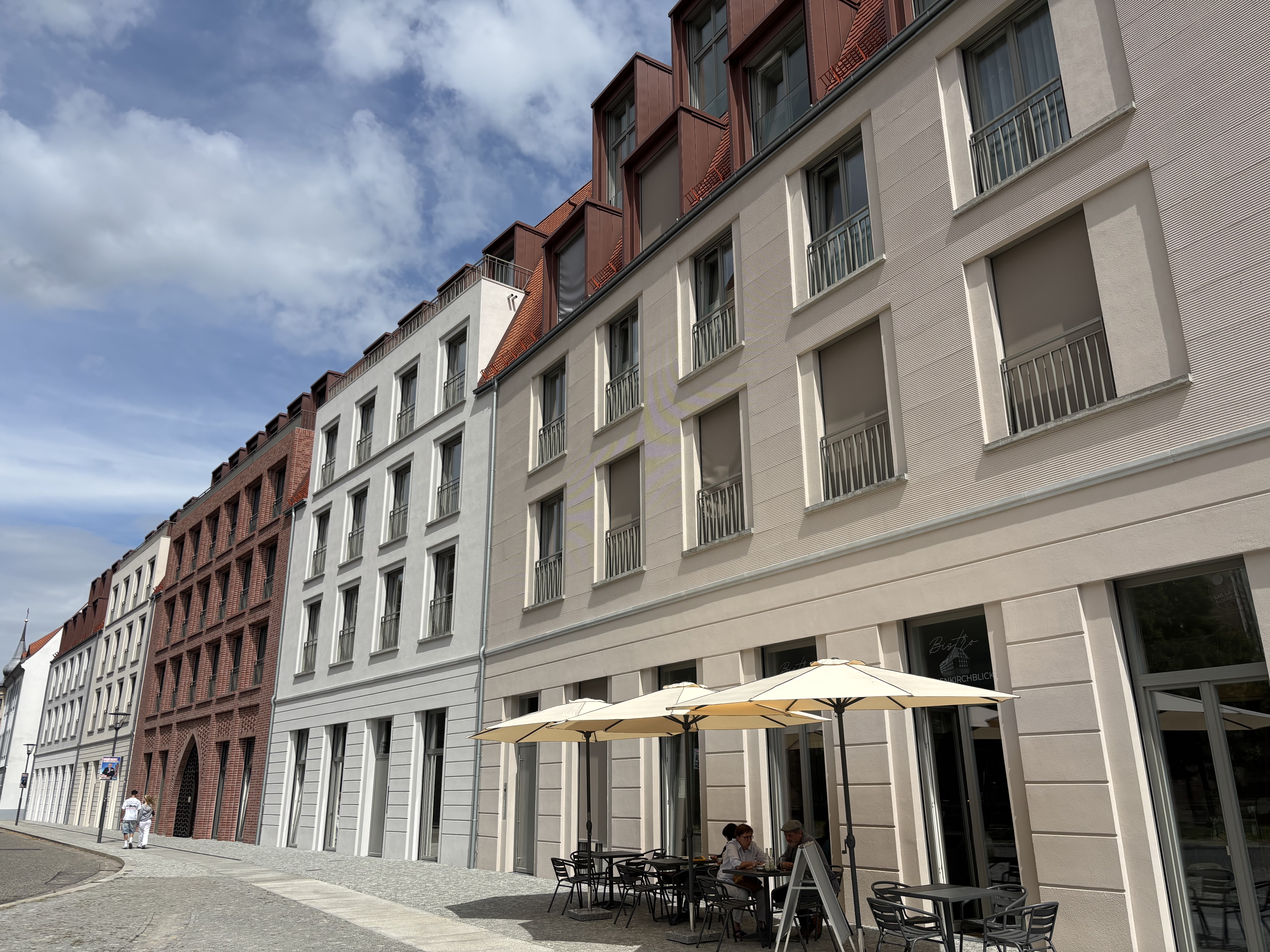 Fassade vom Neubaugebäude direkt neben dem Bolfrashaus, hinter der Marienkirche. Ein  Bistro mit Biergartenschirmen ist zu sehen
